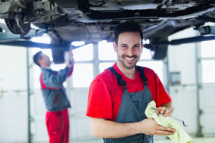 A smiling auto mechanic works under a car, demonstrating practical skills in vet training.