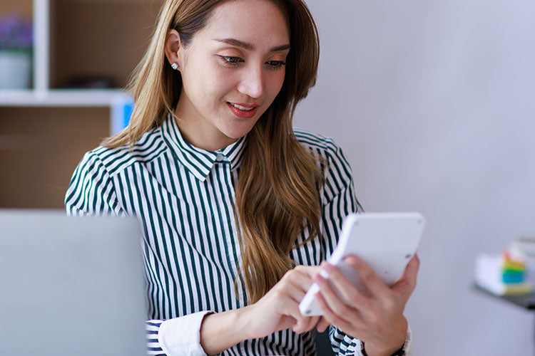 A woman looks at her smartphone while sitting indoors, demonstrating modern learning with vet training resources.